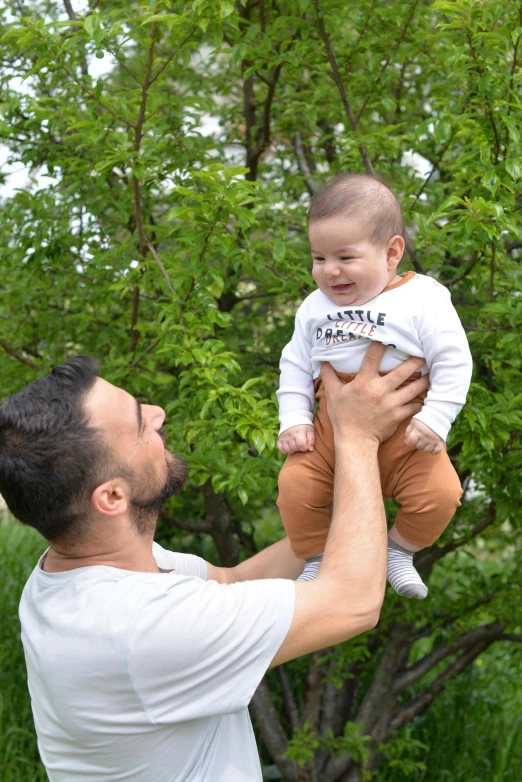 the man holds his baby in the air above trees