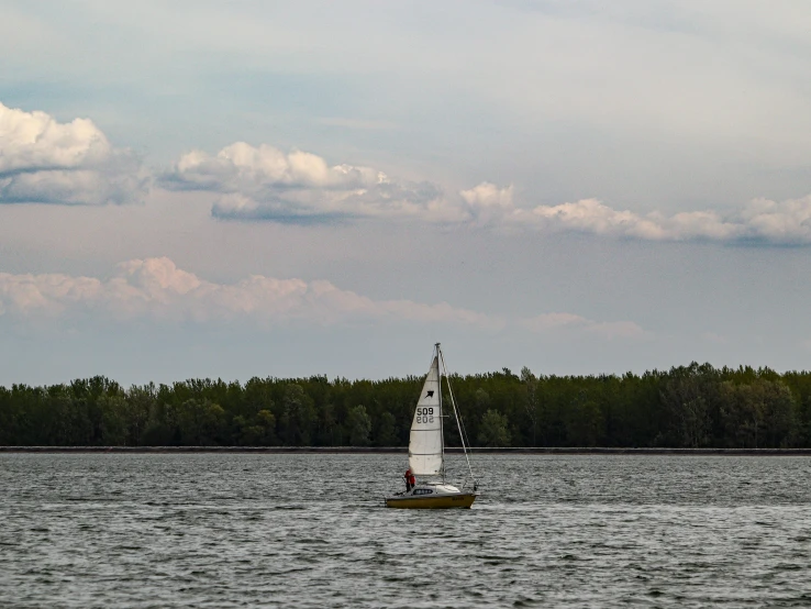 a white sail boat sailing along the shoreline