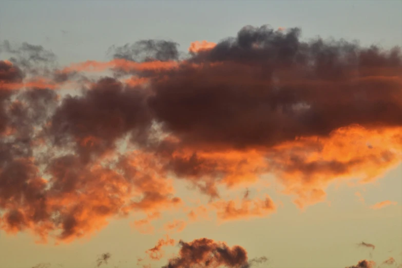 an airplane flying in the sky with orange clouds at dusk