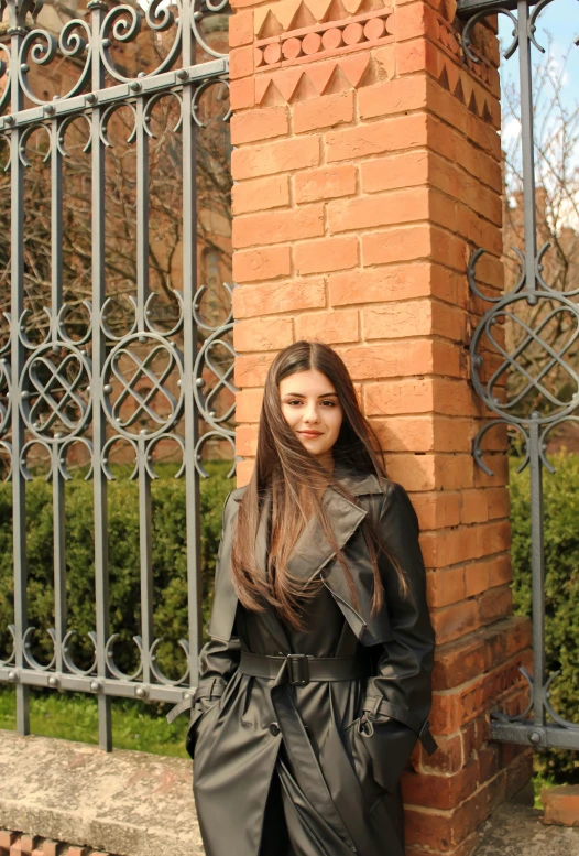 a woman in a long coat posing against a fence