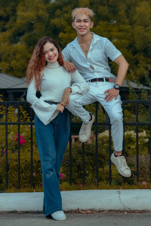 a young man standing next to a young woman on top of a fence