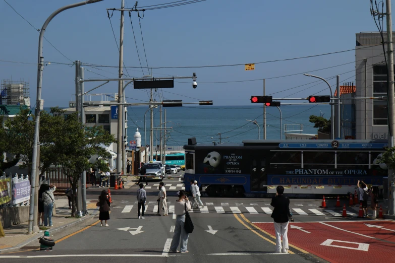 pedestrians on street with bus in middle near sea