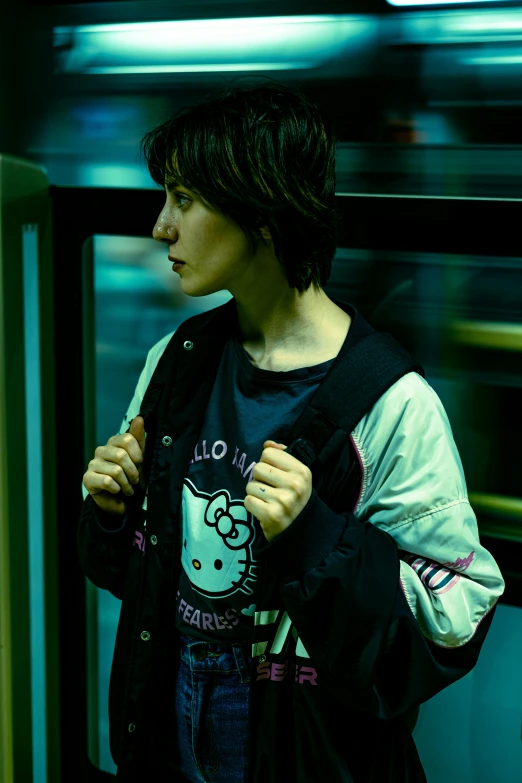 a young man with long hair stands on a train platform and pulls his jacket off