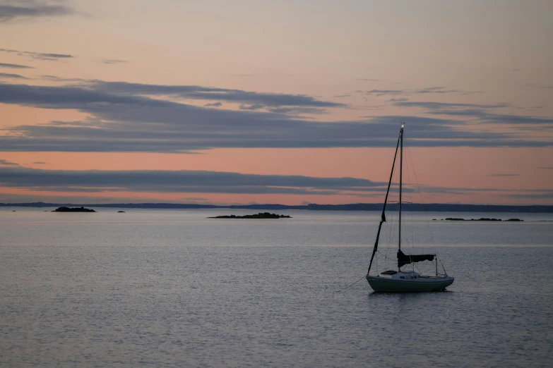 small white sailboat with black sail in an ocean at dusk