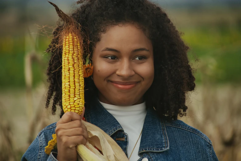 girl in jeans jacket holding up a corn cob