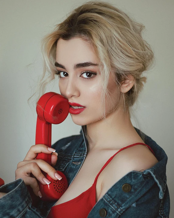 a woman with a blue jean jacket talking on a red telephone
