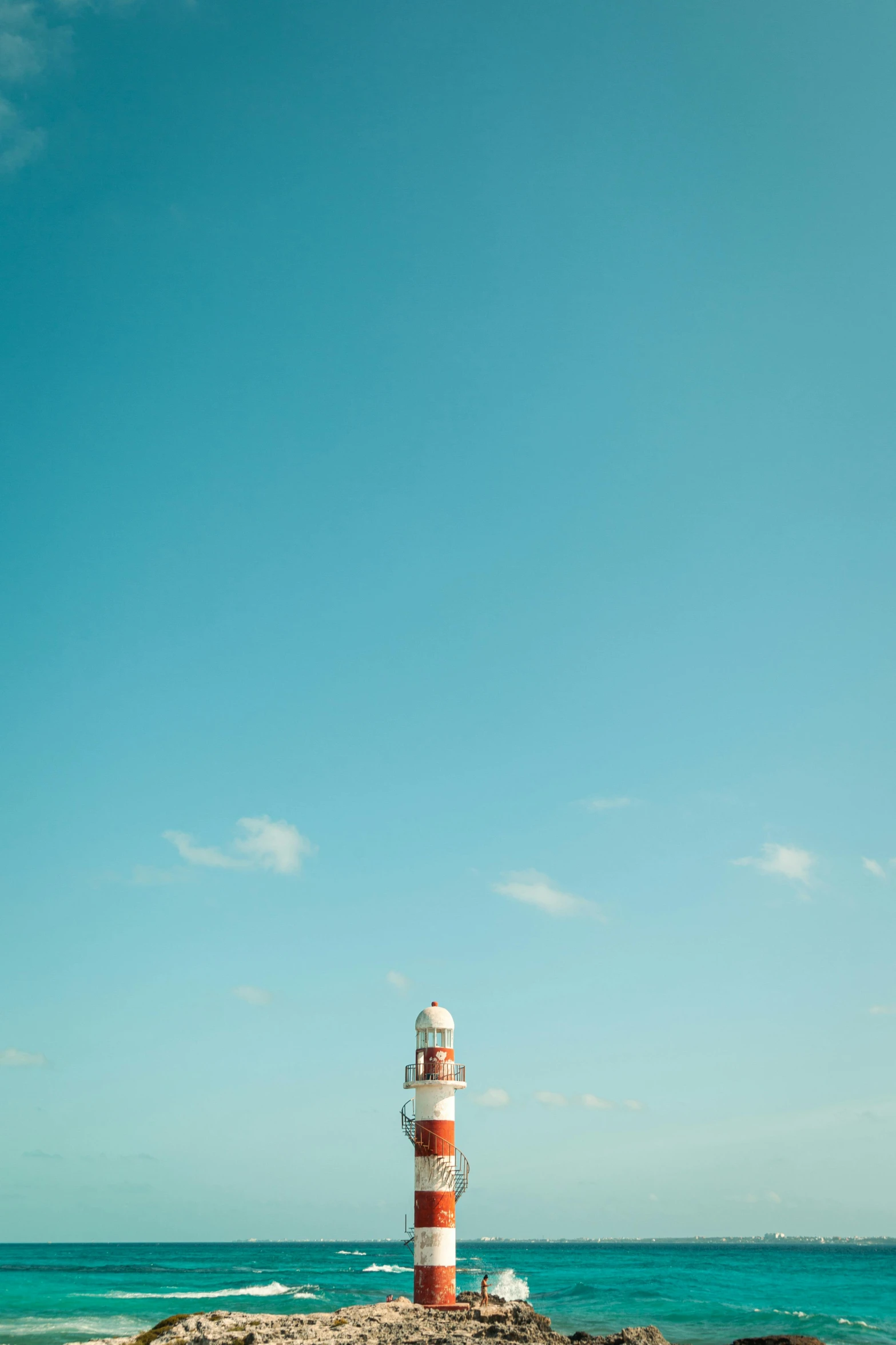 the light house is near the ocean and blue sky