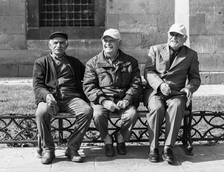 three older men sitting on a bench in front of a stone wall