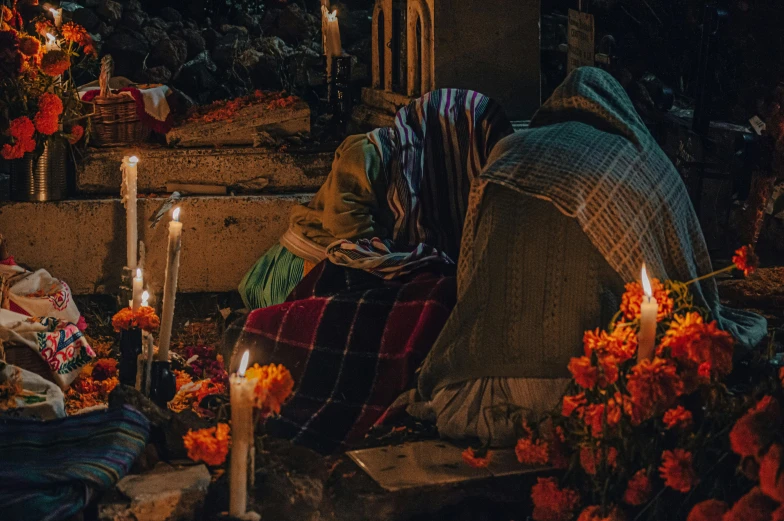 a lady sits in front of a pile of flowers and candles