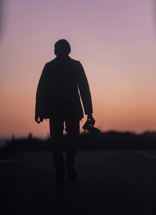 a person is holding their skateboard as they walk through the sunset