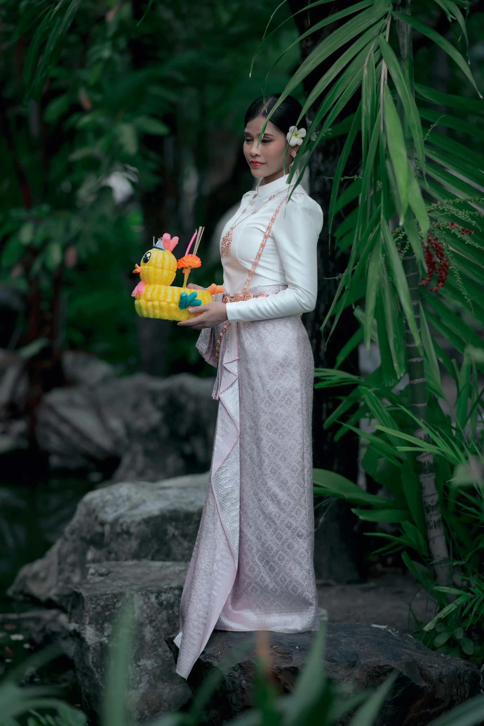 woman in white dress holding pineapples and a bunch of flowers