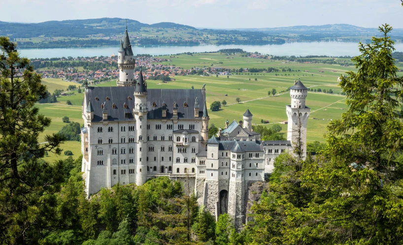 a castle built in the middle of some woods with mountains in the background