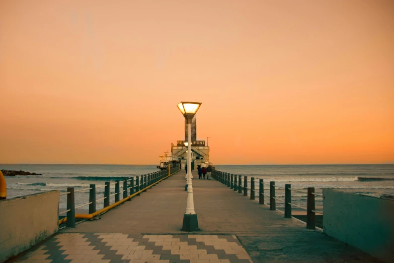 people walk along the pier at sunset on a hazy day