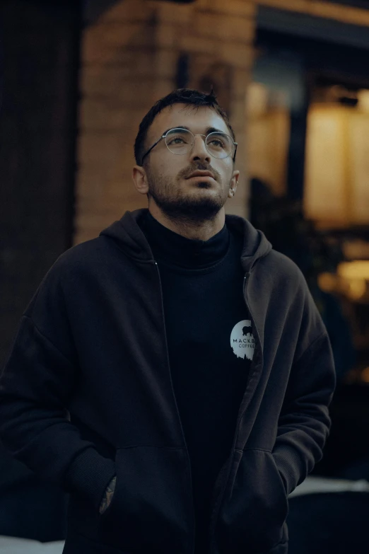 a man in black hoodie looking upward outside of a building