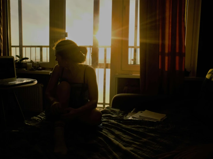 a woman sits on the bed with sun shining in her windows