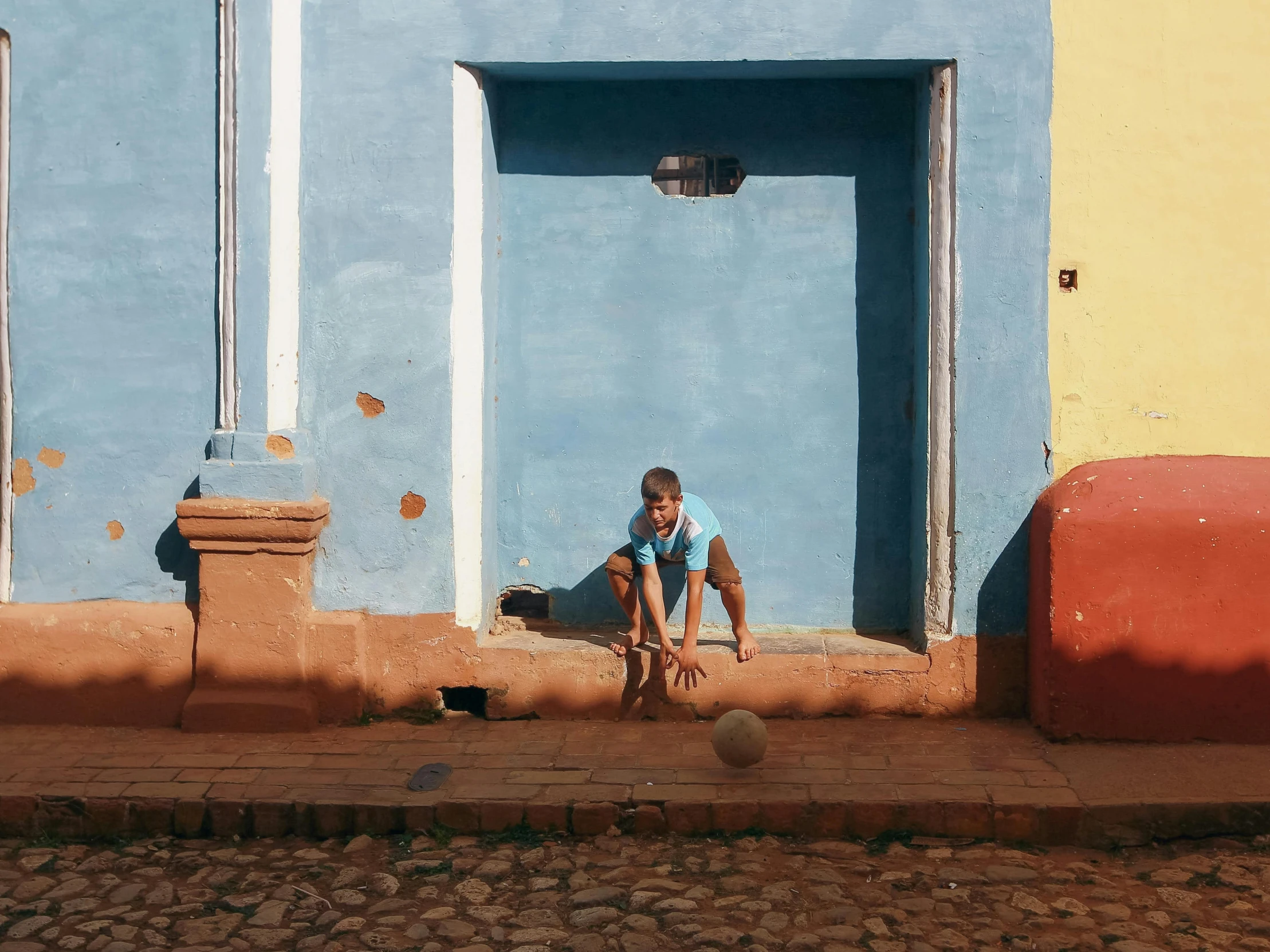 a young child sits on the curb by a wall