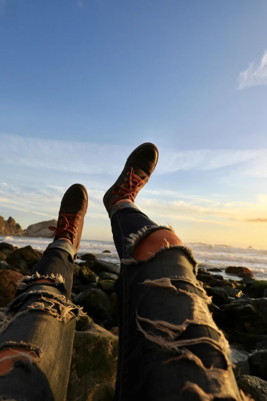 a person wearing dirty jeans and socks standing on top of rocks