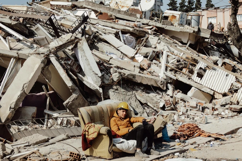 a man in yellow jacket sitting on chair surrounded by rubble