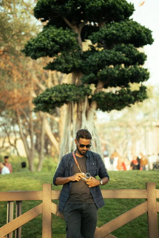 a man holding a camera looking at his phone while standing next to a fence