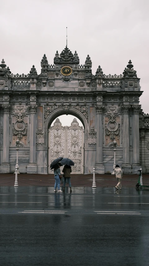 two people walking in the rain, holding umbrellas, under an arch