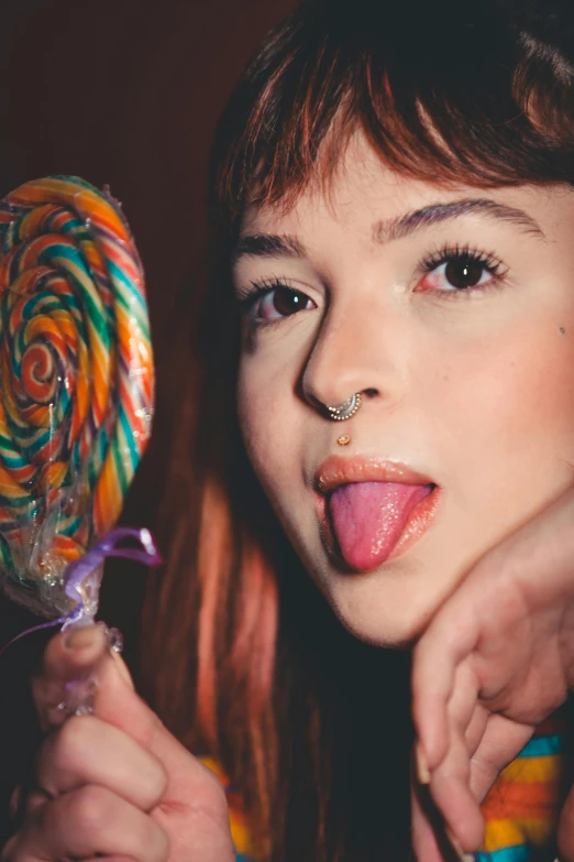 a  holding up an orange lollipop with her tongue