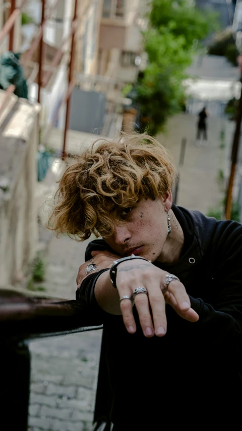 a man with curly hair holding his hand near the top of a railing