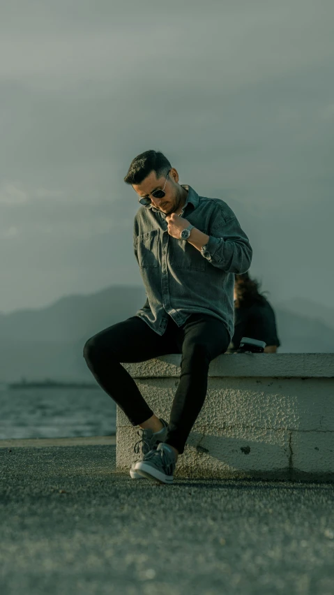 a man sitting on a concrete block with his hand up to his ear