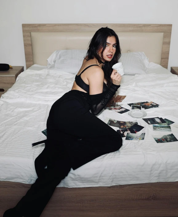 woman holding beverage on bed with pictures spread out across the bed