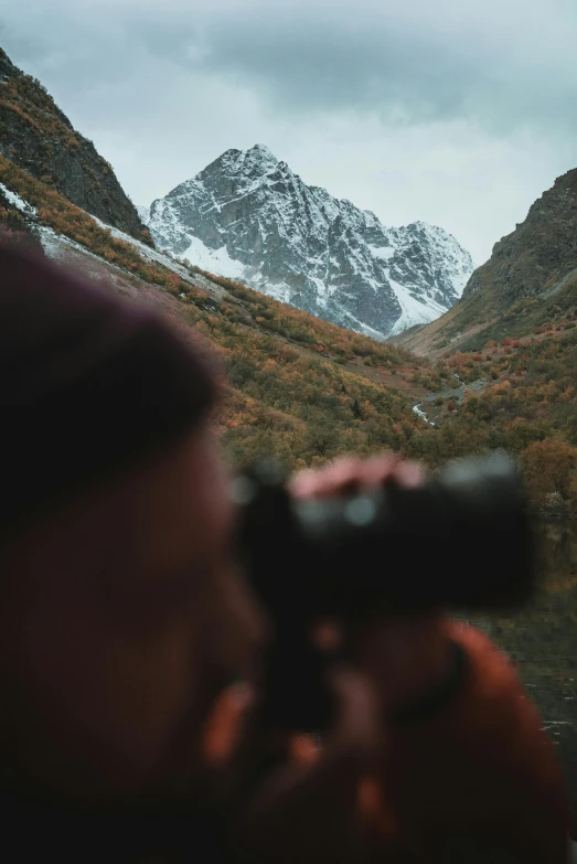 a man looking through a telescope at a mountain range