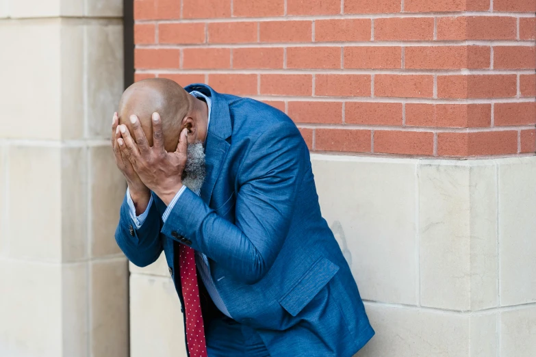 the man is leaning up against the wall holding his head