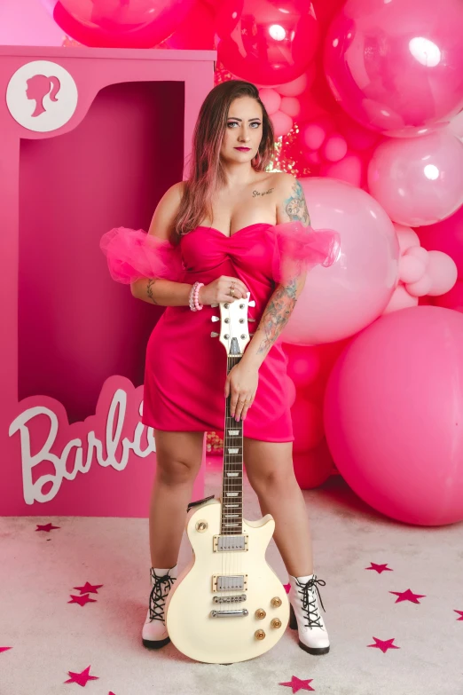 a woman poses with a guitar in front of some balloons