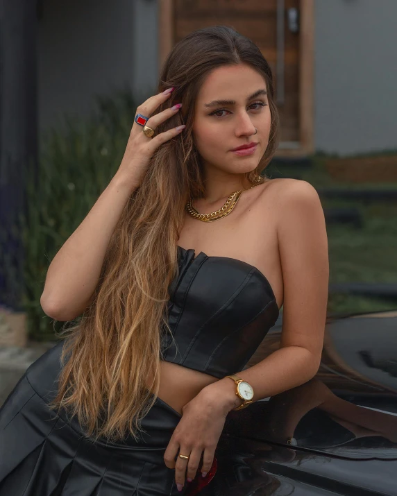 a girl in a black dress is leaning on a car