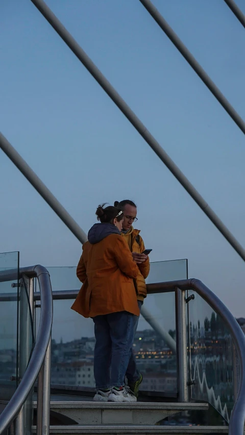 a man and woman in orange jackets standing on the railing