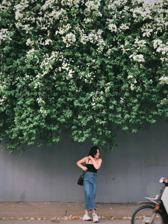 a woman standing by a tree in front of a wall