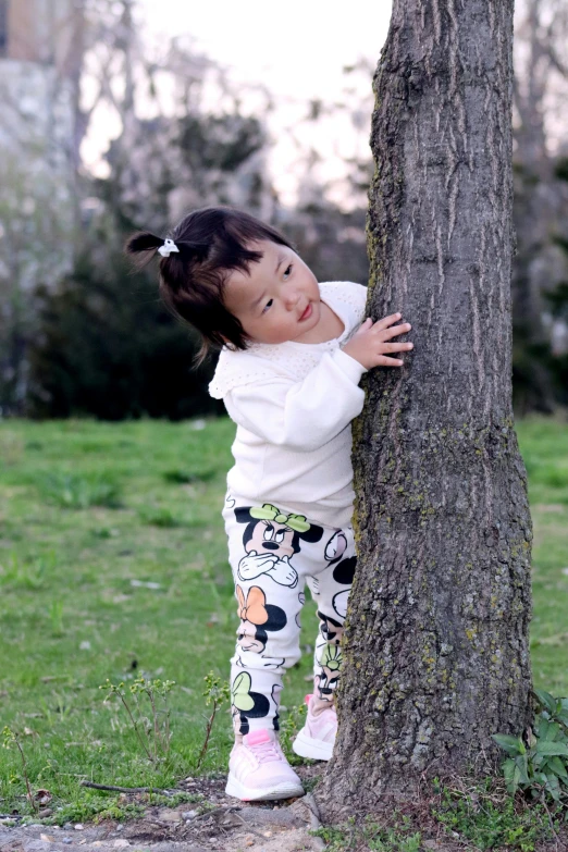 a girl leaning on a tree with a white shirt and black and yellow pants