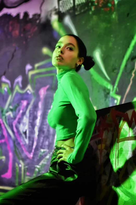 a girl leaning on a wall with a graffiti wall behind her