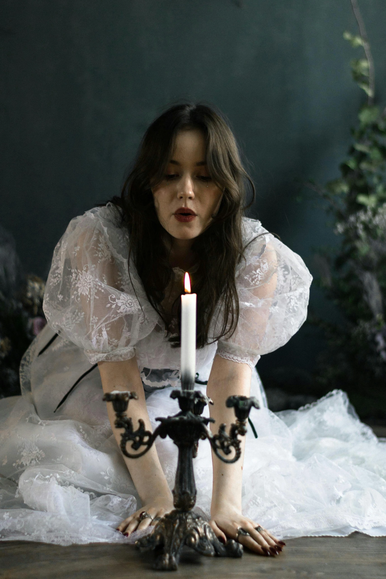 a woman in white dress and black candles is crouched down with her hands around a pillar