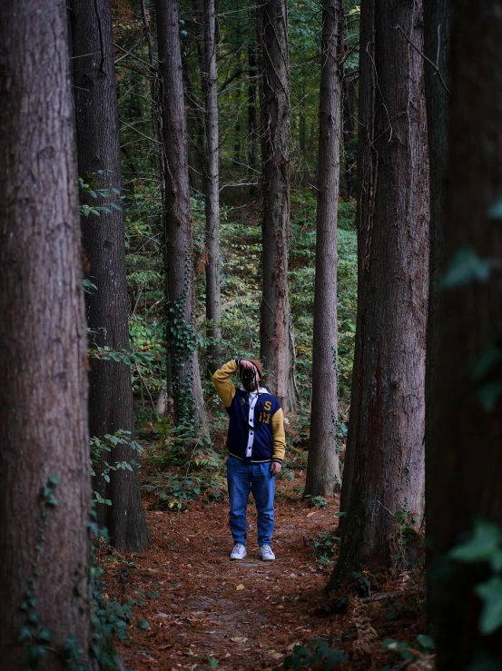 man in the woods with an umbrella, standing in front of some trees