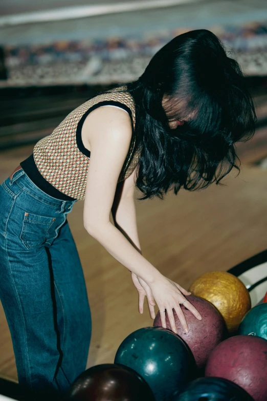 a young woman reaching down into a bowling ball basket