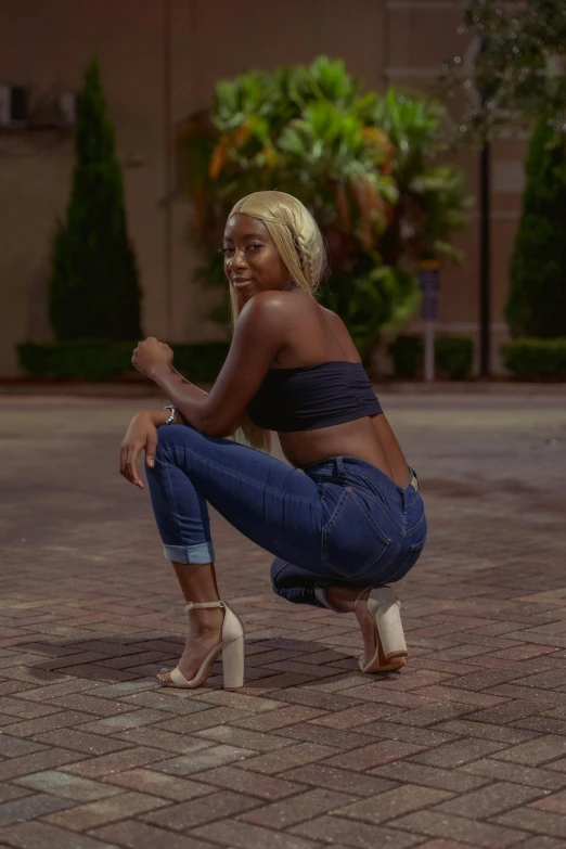 a smiling woman wearing jeans kneels down to her knees