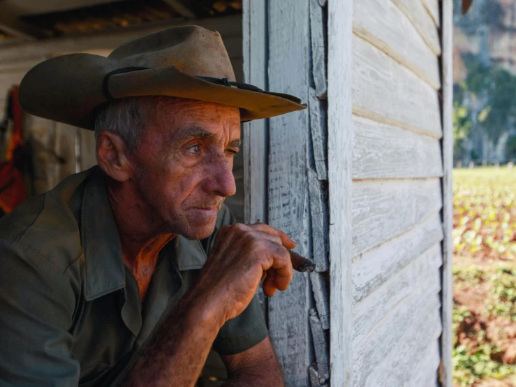 an old man in a cowboy hat leans against a door