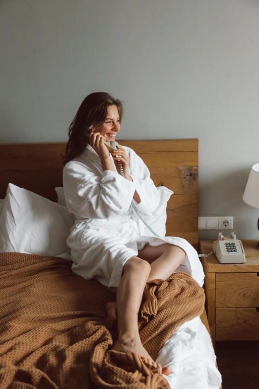 a woman sitting in bed wrapped in white towels talking on a cell phone