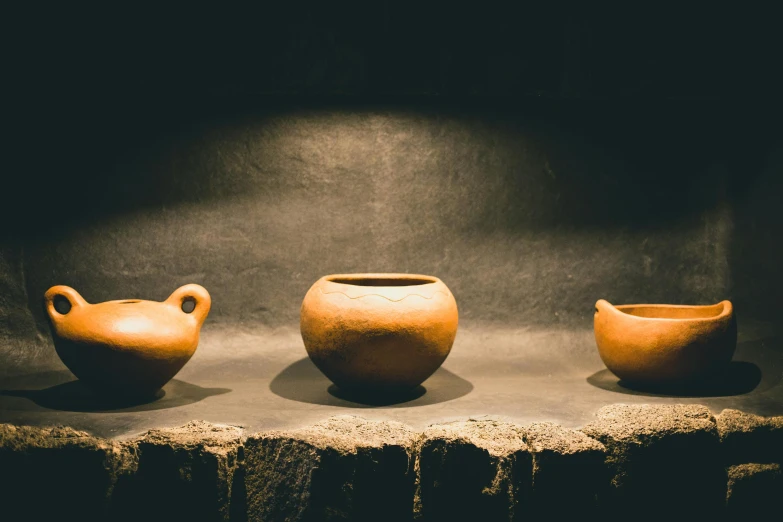 three small clay jars are on display on a stand