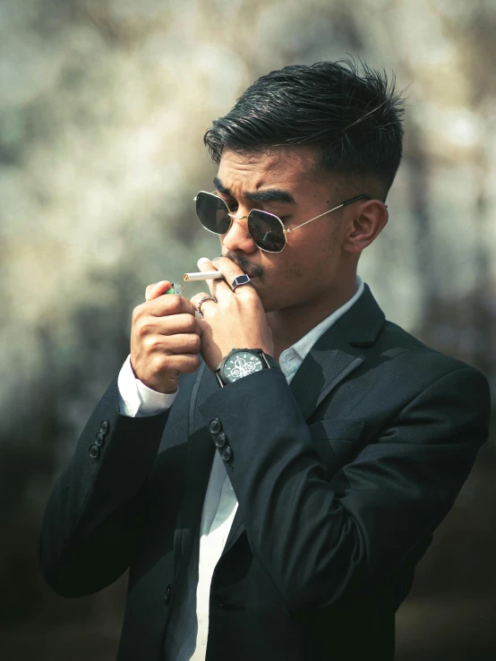 a young man in a suit and glasses smokes a cigarette