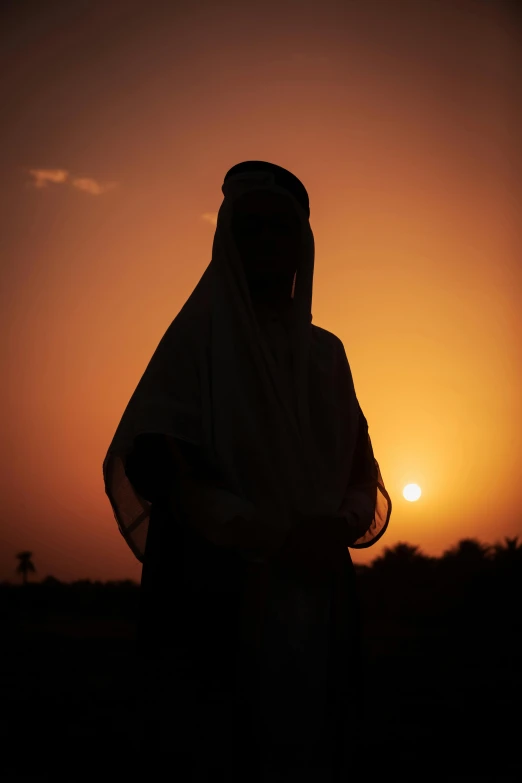 a person wearing a veil is silhouetted against the sunset