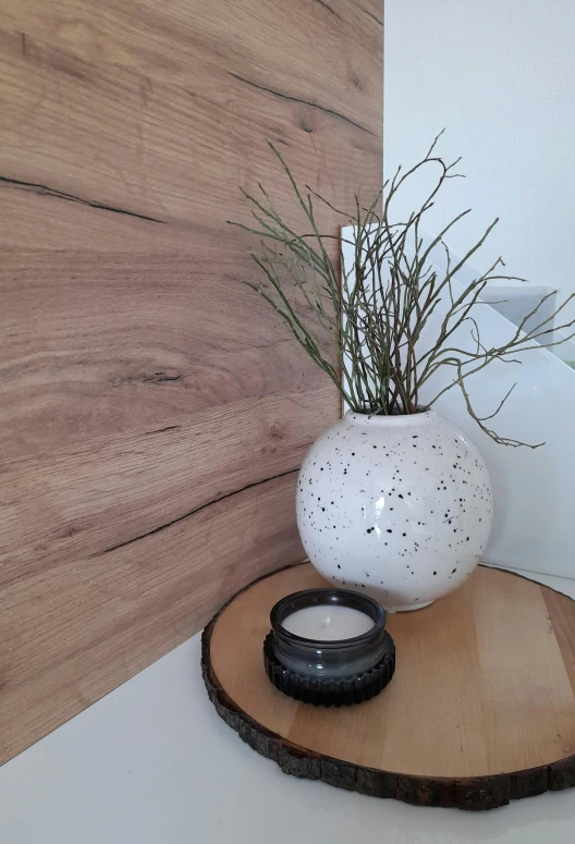 a white vase with grass and water on a wooden tray