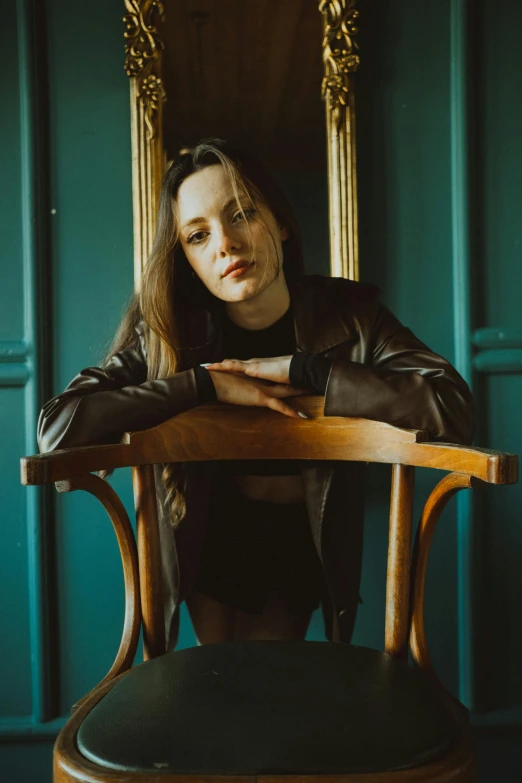 a girl in leather jacket sitting at wooden chair