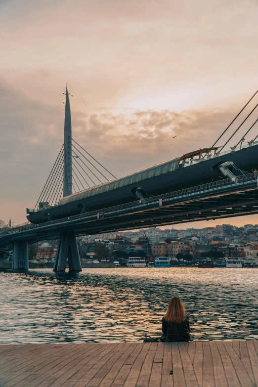 the woman is sitting on the dock looking at the bridge