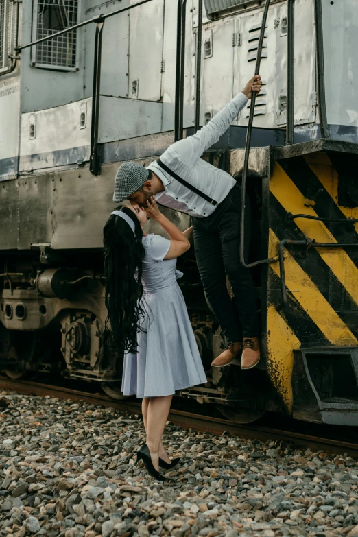 a man and woman standing on train track while the woman stands at the door with an umbrella