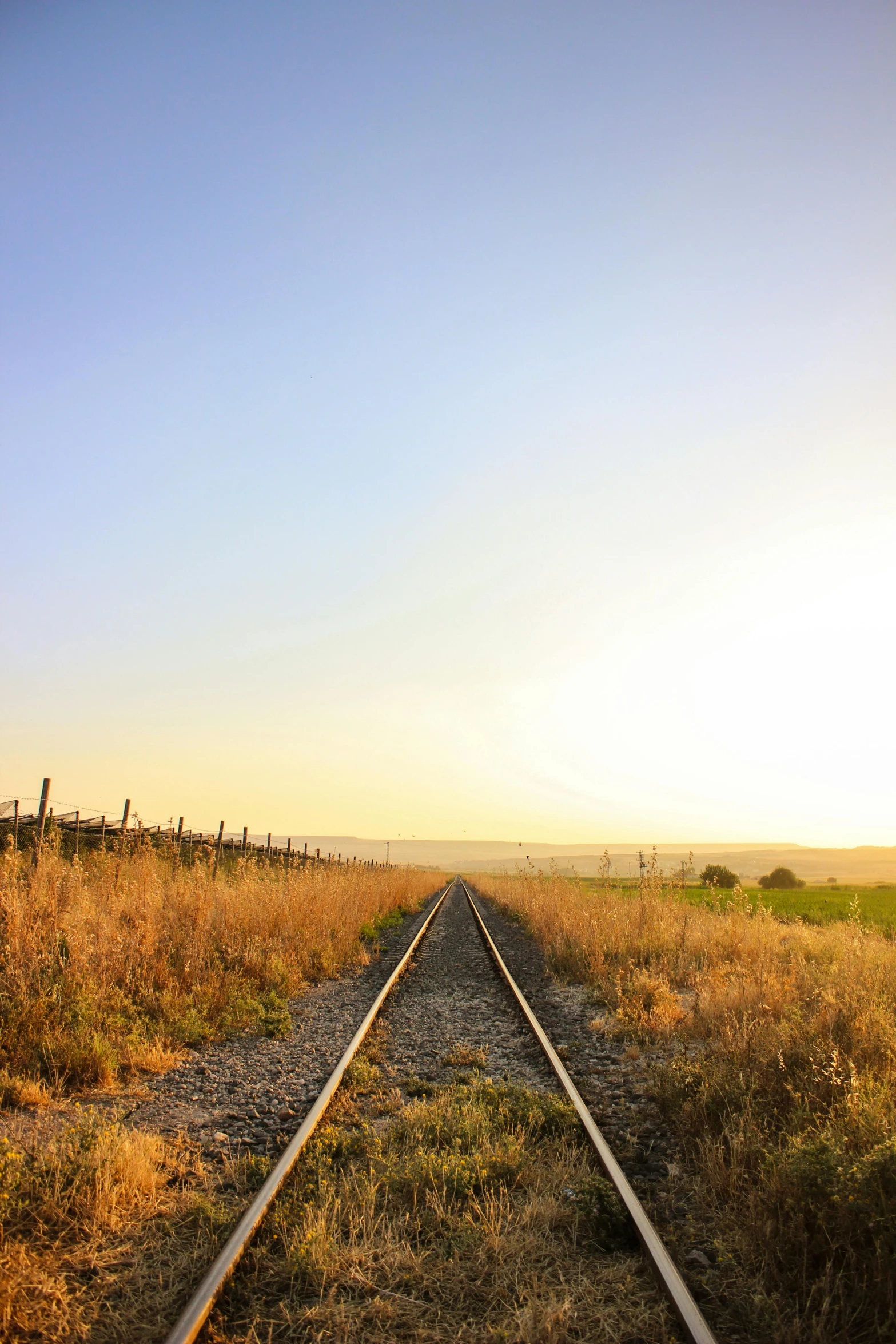 railroad track with grassy plain in the background at sunset